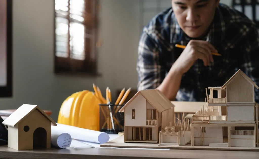 Engineer examining architectural models and construction plans on a desk, with tools and a hard hat nearby, reflecting R&A Industries' focus on new construction and reliable system installations.