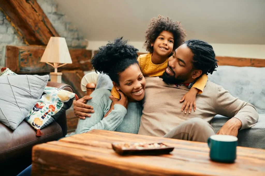 Happy Black family enjoying quality time together at home, sitting on a couch with a cozy atmosphere, showcasing a relaxed and loving environment.