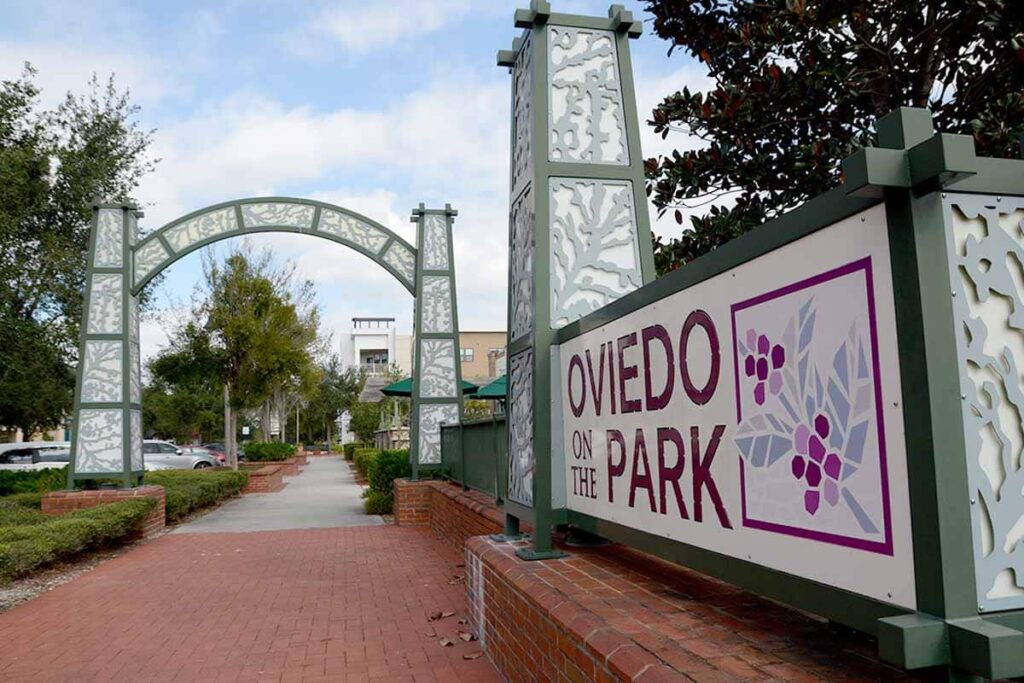 Oviedo on the Park entrance sign with decorative archway, surrounded by greenery and brick pathway, highlighting the community's local charm and connection to R&A Industries' backflow testing services.