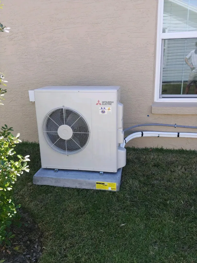Mitsubishi Electric heat pump unit installed outside a home in Oviedo, Florida, surrounded by grass and shrubbery, illustrating heat pump service offerings by R&A Industries.