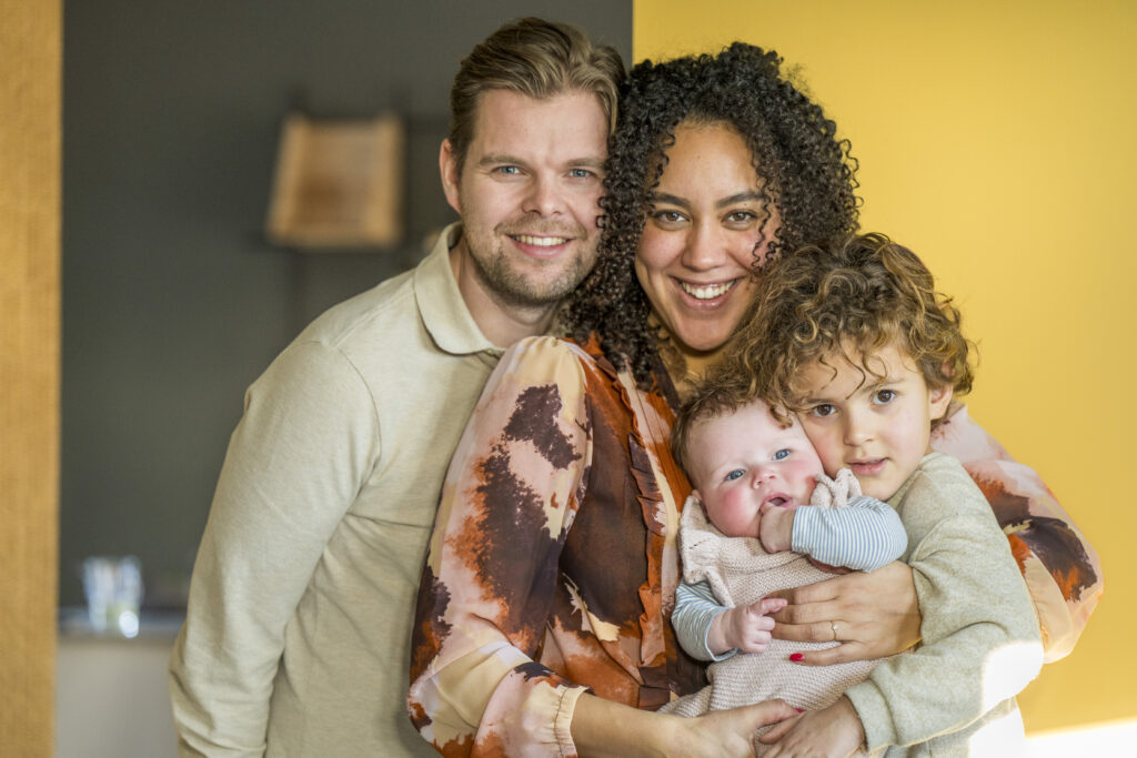 Happy family of four embracing at home, showcasing warmth and joy, with parents holding their children, emphasizing family safety and care in a cozy environment.