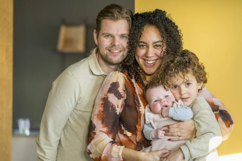 Happy family portrait with two parents and their two children, one a baby. Backflow testing ensures safe water for families.