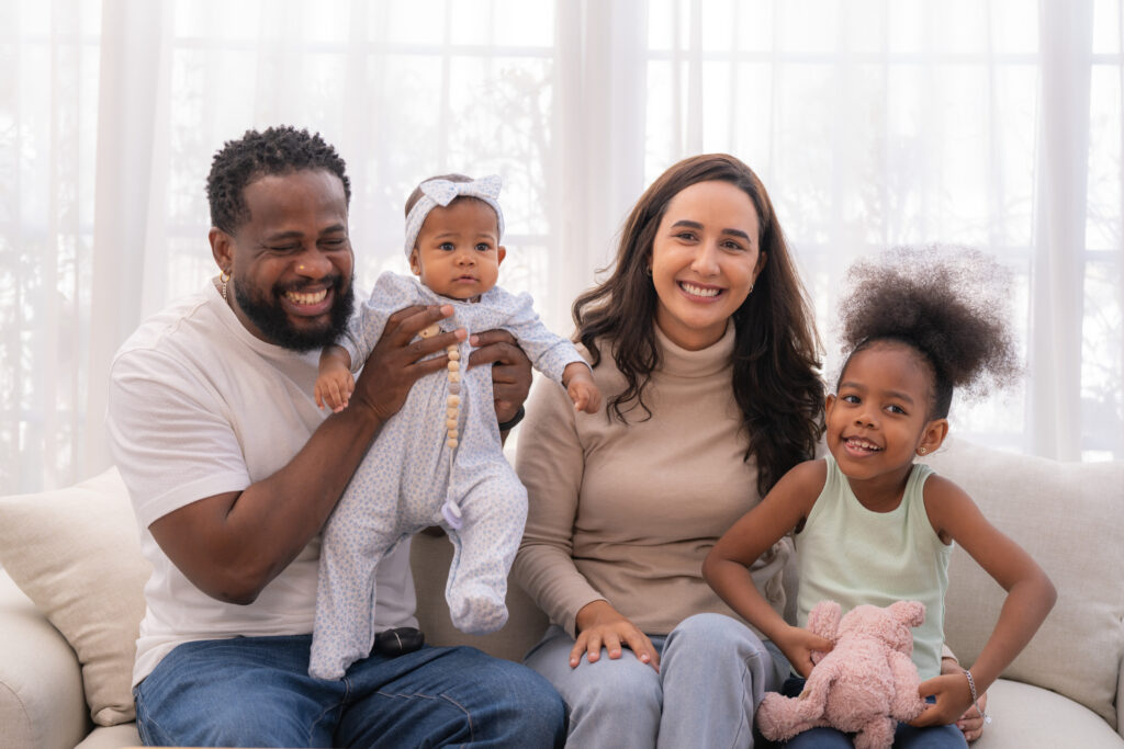 Happy family portrait with two parents and two daughters sitting on a couch. Toilet Clog Repair not needed here.