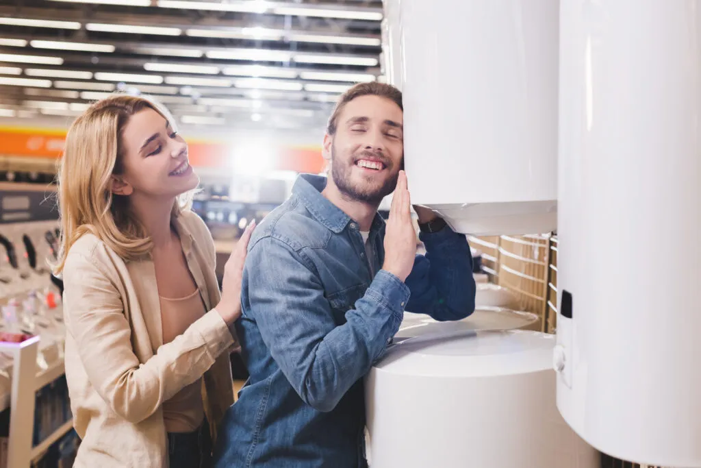 Happy couple shopping for a new furnace. Man leans on a white furnace with a smile, woman looks on, Oviedo, FL. Heating solutions.