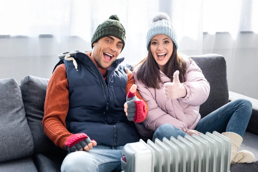 Happy couple with thumbs up near a heater. Heating maintenance ensures warmth and comfort in Oviedo, FL during the cold season.