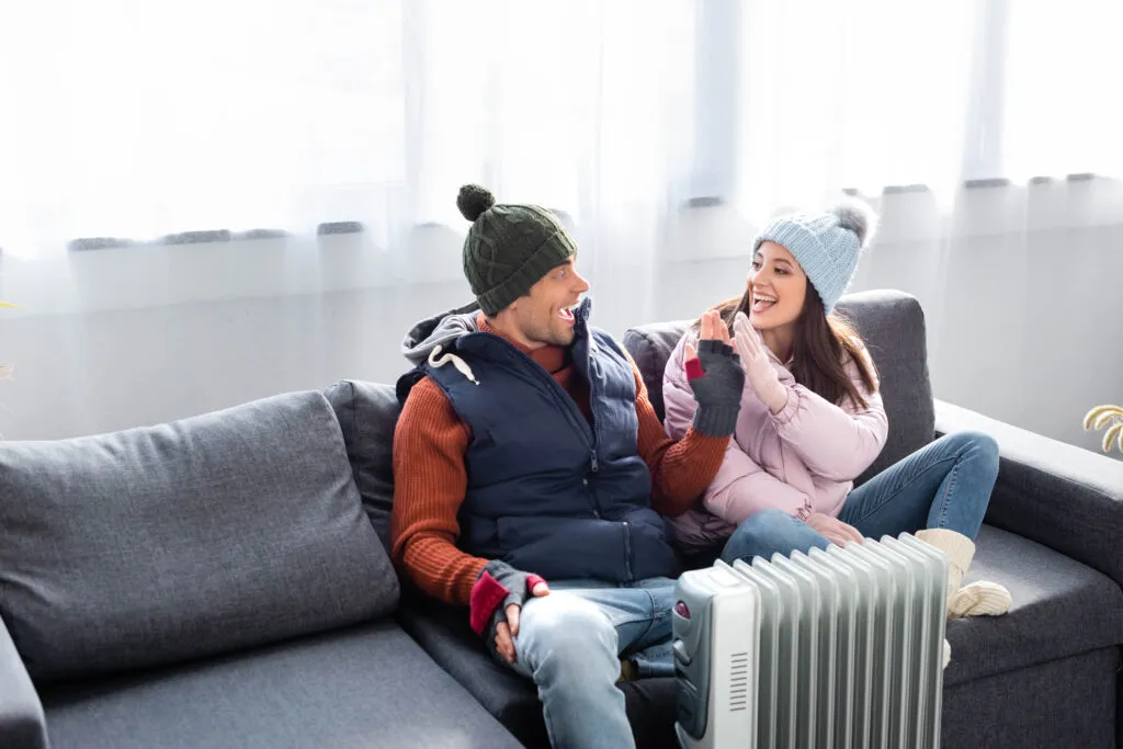 Couple in winter clothes near heater. Consider heat pump repair in Oviedo, FL, for efficient home heating solutions. Stay warm this winter!