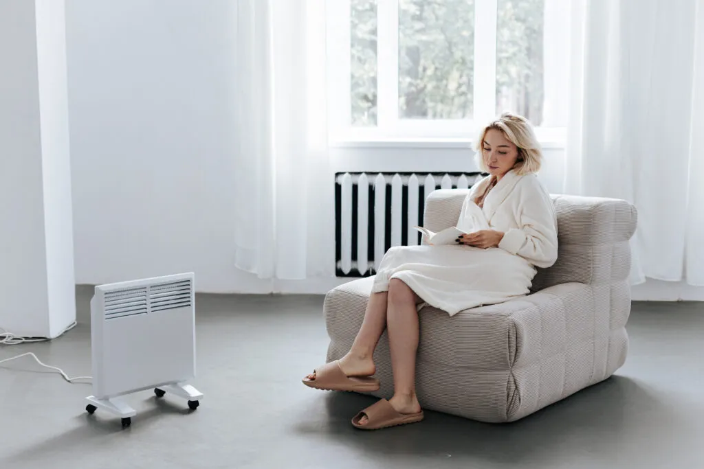 Woman reading near a heater. Heat pump maintenance ensures optimal heating performance. Stay cozy in Oviedo, FL.