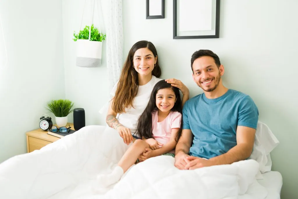 Happy family smiling in their bedroom, possibly after getting Duct Cleaning in Orlando, FL, creating a healthy home environment for everyone.