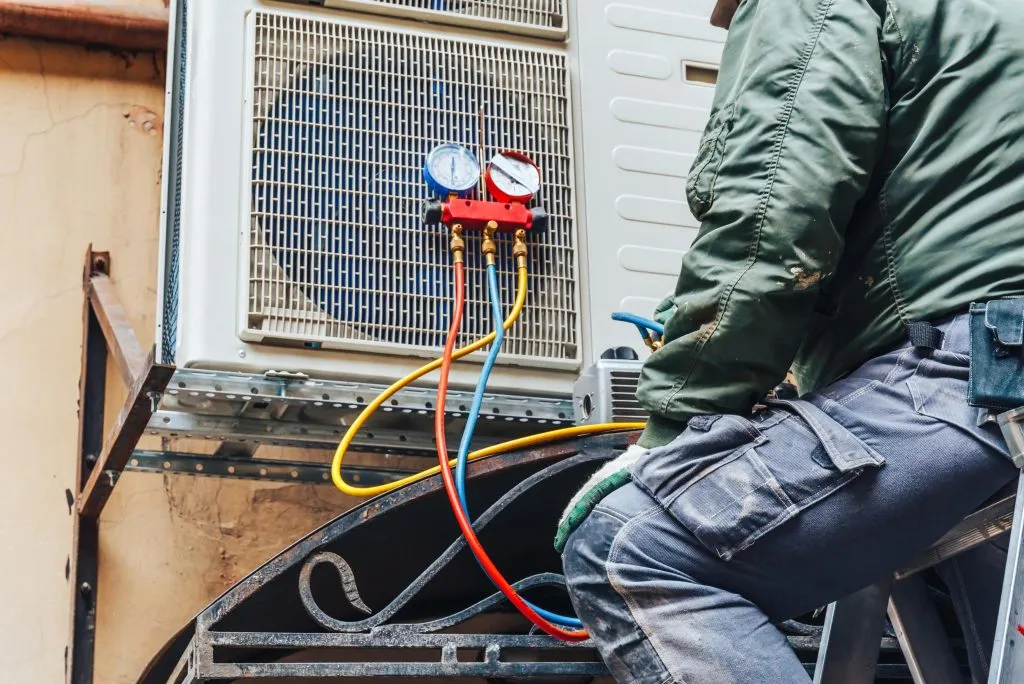 HVAC technician performing heating installation and replacement services using gauges on an outdoor unit, ensuring optimal performance.
