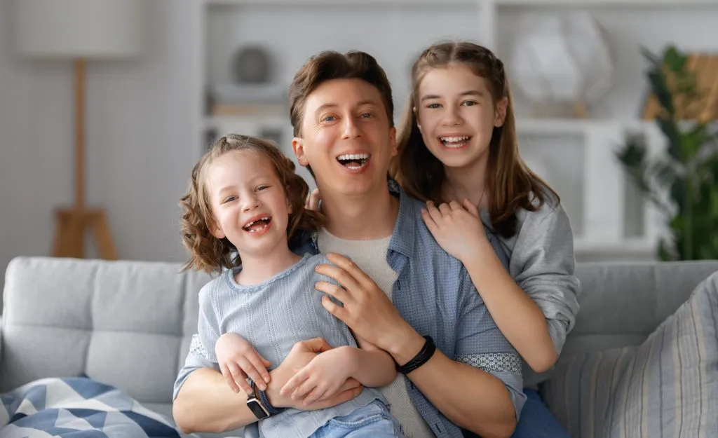 Happy family portrait; father with two daughters smiling, promoting comfort indoors like with reliable Heating Installation in Oviedo, FL.