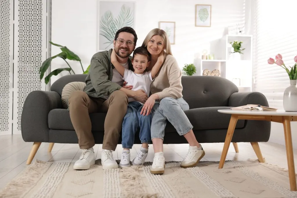 Happy family of three smiling on a couch, creating a warm and inviting atmosphere in their living room, showing how electrical services creates a safe home.